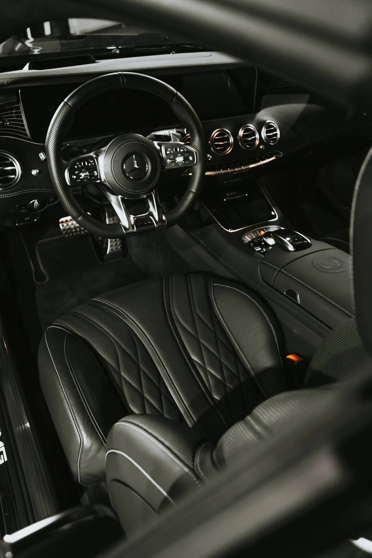Black luxury car interior with leather steering wheel, quilted seats, and illuminated dashboard controls