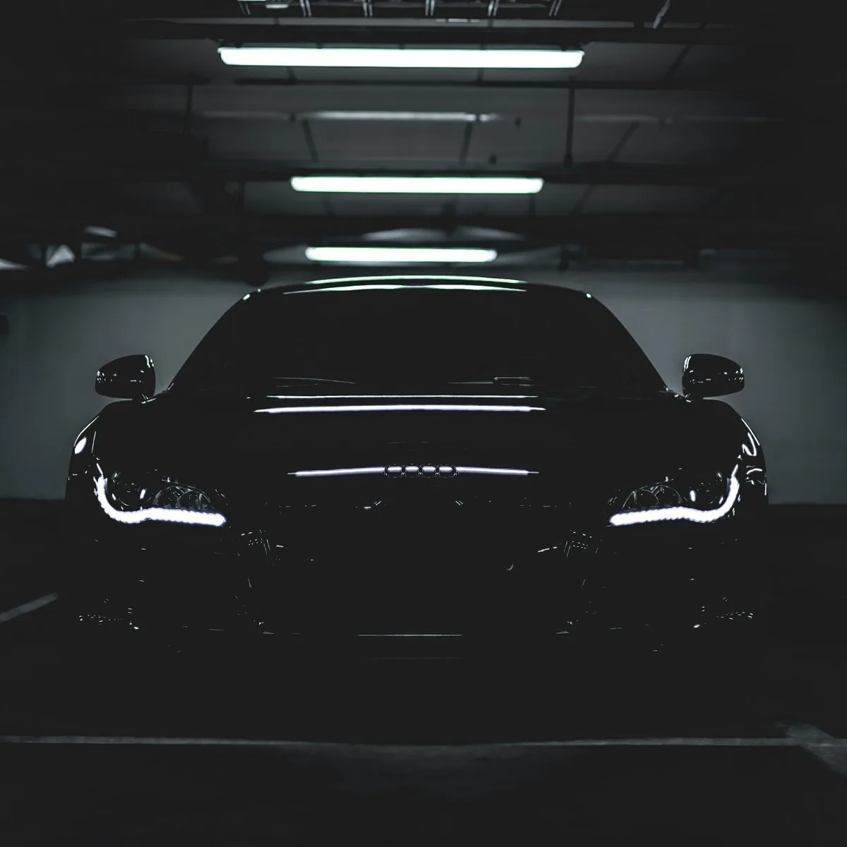 Black sports car front view in a dark garage with LED headlights illuminated and ceiling lights above