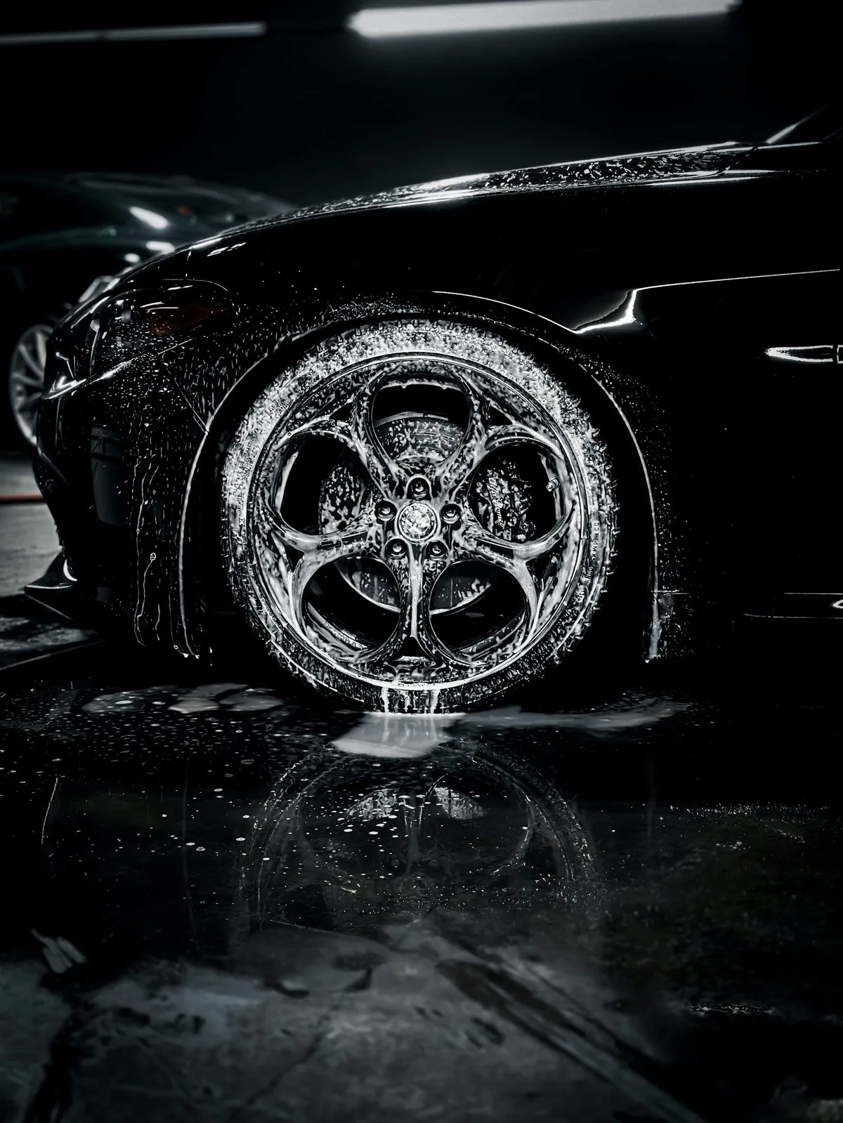 Close-up of wet car wheel and tire with intricate alloy rim design, dramatically lit against dark background