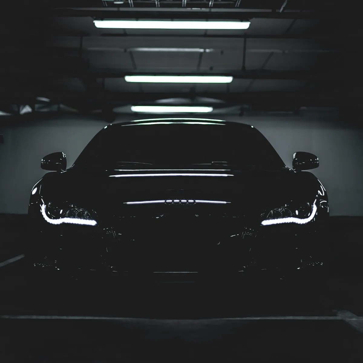Black sports car front view in a dark garage with LED headlights on