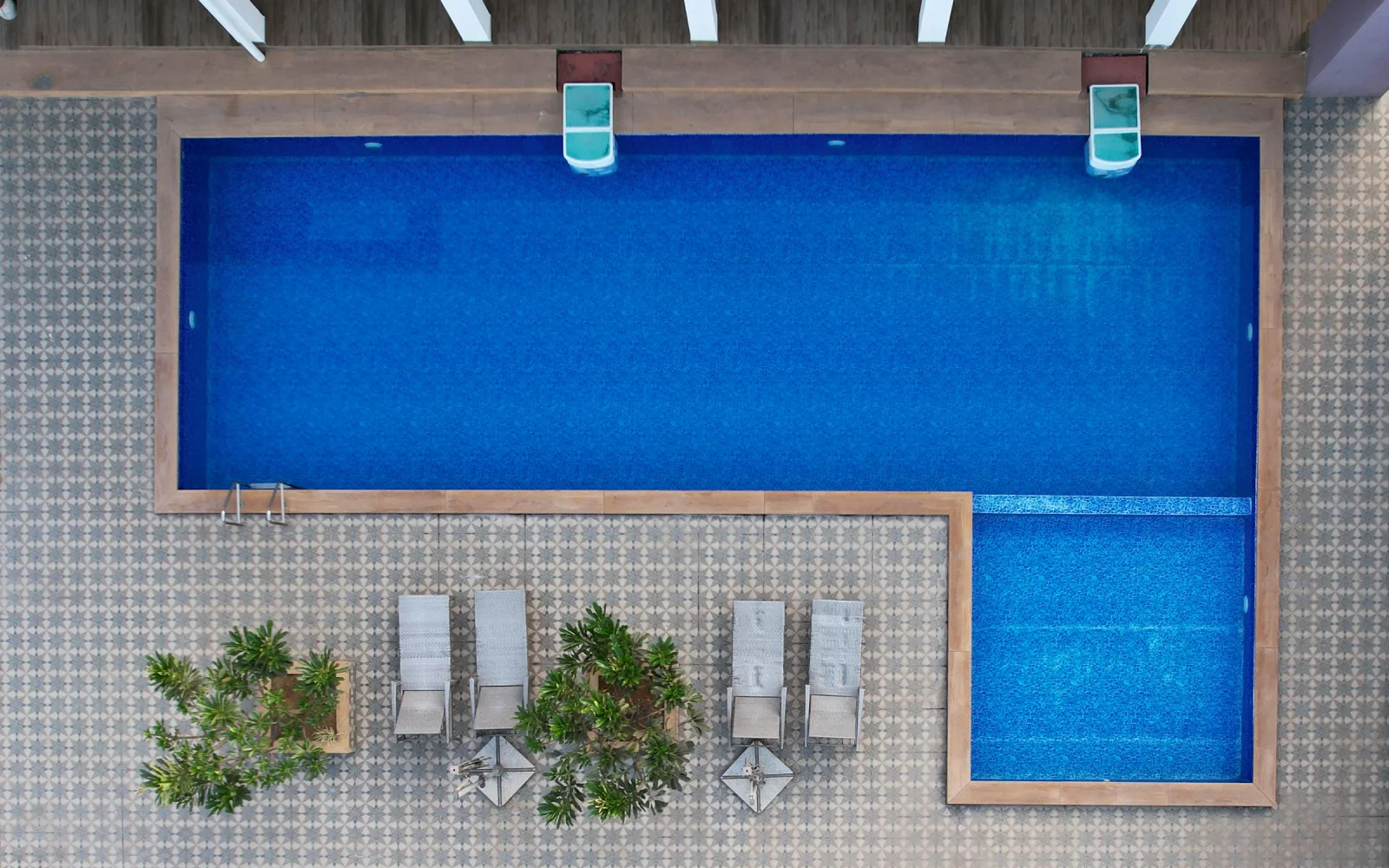 The same pool built: deep blue water, timber coping, a porcelain deck, four loungers and planters